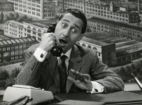 Scena del film "Domenica è sempre domenica" - Regia Camillo Mastrocinque, 1958 - In un ufficio, mezza figura di Alberto Sordi seduto a una scrivania mentre parla al telefono con occhi e bocca spalancati.