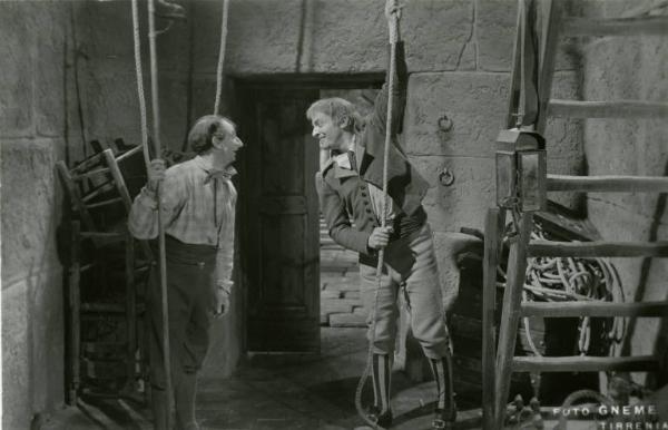 Scena del film "Don Buonaparte" - Regia Flavio Calzavara, 1941 - Totale. Osvaldo Valenti, a destra, tira una fune che scende dall'alto e sorride a un attore non identificato.