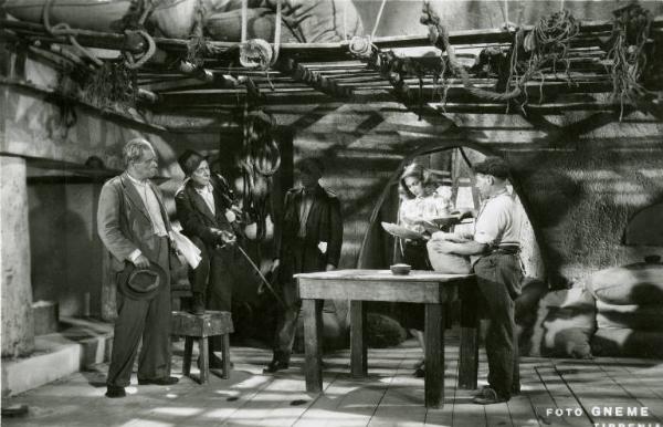 Scena del film "Don Buonaparte" - Regia Flavio Calzavara, 1941 - In un granaio, Oretta Fiume tiene un piatto con una mano mentre osserva qualcosa che ha nell'altra. Attorno a lei, ci sono quattro uomini.