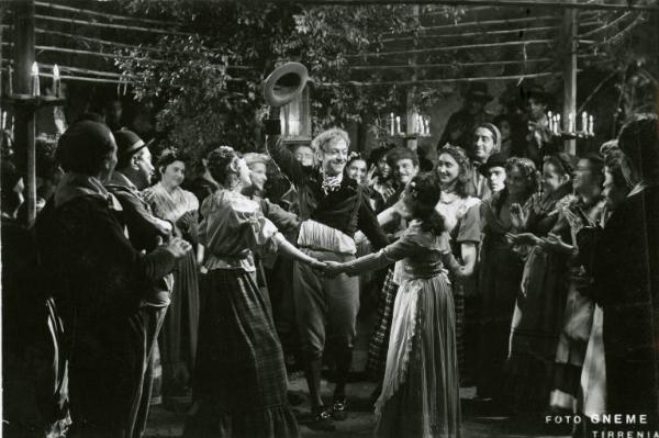 Scena del film "Don Buonaparte" - Regia Flavio Calzavara, 1941 - Totale. Al centro Osvaldo Valenti balla in mezzo a delle ragazze che si tengono le mani come in un girotondo. Intorno a loro altri donne e uomini.