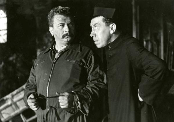 Scena del film "Don Camillo" - Regia Julien Duvivier, 1952 - Mezza figura di Gino Cervi in tuta da meccanico e di Fernandel, con i pugni sui fianchi, che lo guarda con il sopracciglio alzato.