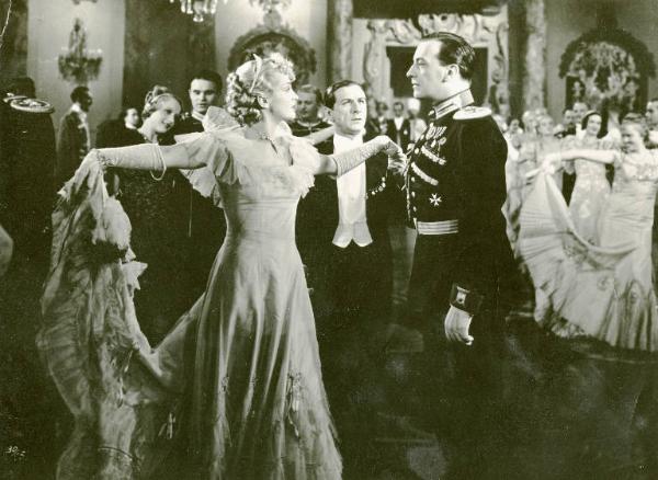 Scena del film "La donna amata" - Regia Georg Jacoby, 1937 - Camilla Horn, con le braccia aperte a croce, tiene con una mano lo strascico del vestito e con l'altra mano, quella di IIván Petrovich. Dietro di loro, Tibor von Halmay e altri invitati.