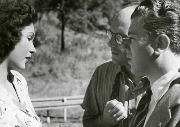 Sul set del film "Diagnosi" - Regia Ferruccio Cerio, 1942 - Mezza figura di profilo di Gino Cervi e Ferruccio Cerio mentre parlano con Luisa Ferida di fronte a loro.