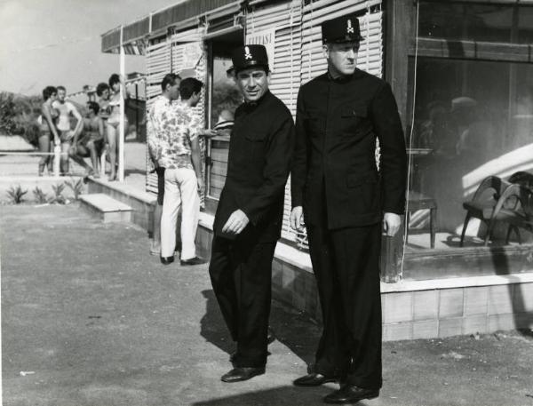 Scena del film "Una domenica d'estate" - Regia Giulio Petroni, 1962 - Totale. Ugo Tognazzi e Raimondo Vianello in livrea da necrofori in uno stabilimento balneare.