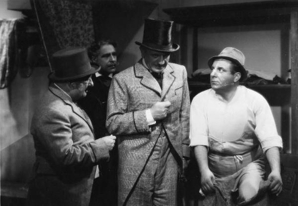 Scena del film "La donna perduta" - Regia Domenico Gambino, 1940 - Alberto Capozzi stringe il pugno davanti al petto. A destra, Carlo Campanini, si infila i pantaloni. A sinistra e sullo sfondo, due attori non identificati.