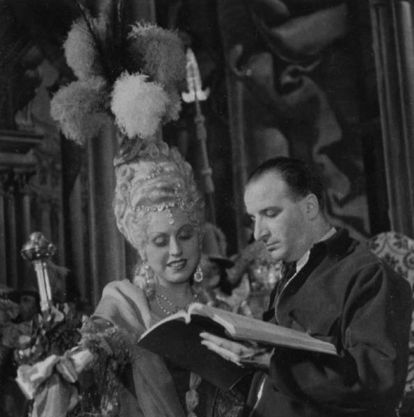 Sul set del film "Don Pasquale" - Regia Camillo Mastrocinque, 1940 - Un attrice non identificata, seduta accanto a Camillo Mastrocinque, guarda il copione che il regista tiene in mano.