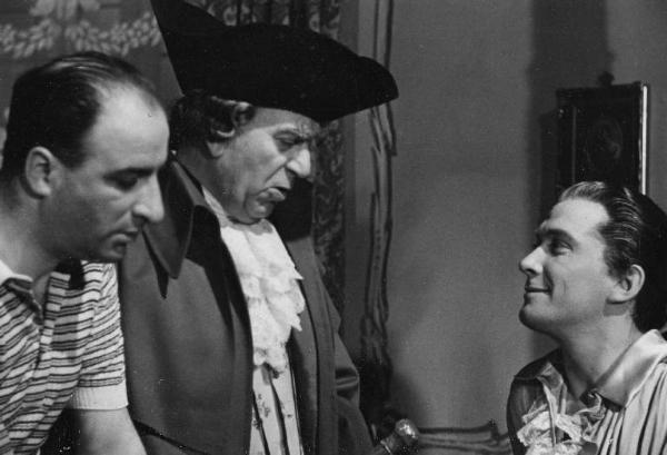 Sul set del film "Don Pasquale" - Regia Camillo Mastrocinque, 1940 - Mezza figura di profilo di Camillo Mastrocinque, un attore non identificato e Franco Coop.