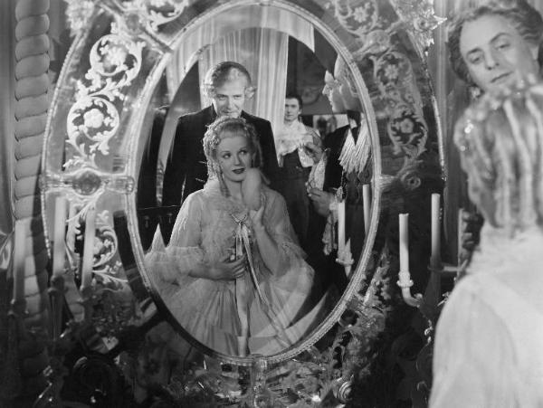 Scena del film "Don Pasquale" - Regia Camillo Mastrocinque, 1940 - Mezza figura frontale di Laura Solari riflessa in uno specchio. L'attrice, si tampona il viso con un piumino da cipria. Alle sue spalle Gino Sabbatini la guarda dallo specchio.
