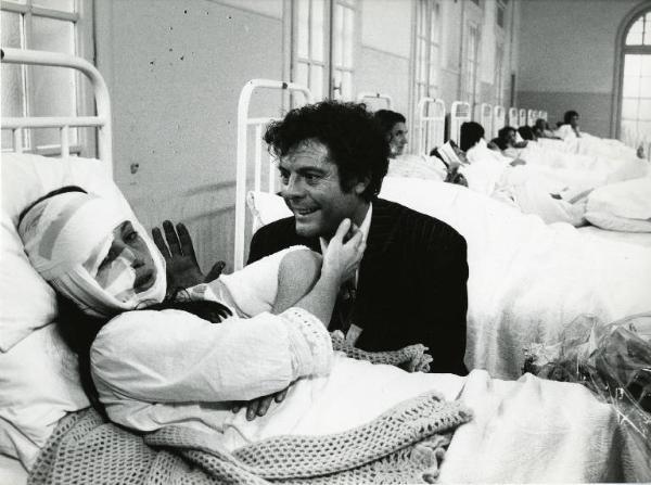 Scena del film "Dramma della gelosia (tutti i particolari in cronaca)" - Regia Ettore Scola, 1970 - Monica Vitti, bendata, in un letto di ospedale. Al suo fianco, seduto, Marcello Mastroianni pare scherzare.