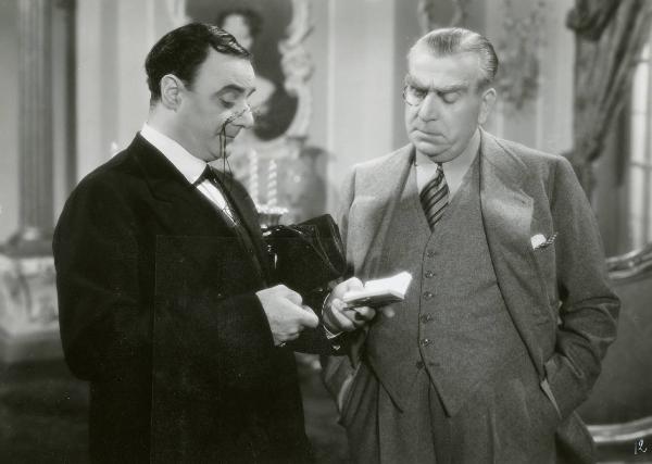 Scena del film "Due cuori sotto sequestro" - Regia Carlo Ludovico Bragaglia, 1941 - Mezza figura di Virgilio Riento, sulla sinistra, e Armando Falconi, sulla destra. Riento tiene in mano un'agenda dalla quale i due attori leggono.