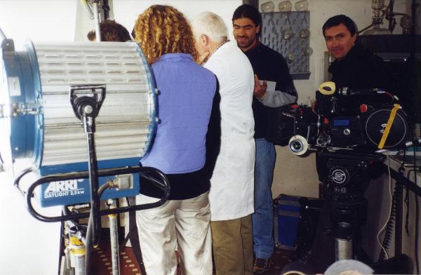 Sul set del film "Due dollari al chilo" - Regia Paolo Lipari, 2000 - Un membro non identificato della troupe guarda nella macchina da presa. Il resto del gruppo, ripreso di spalle, prepara il set del film.