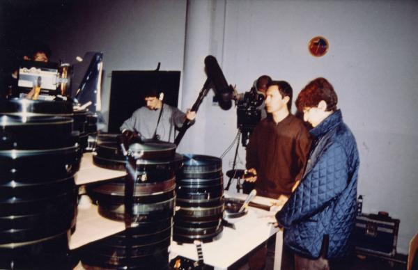 Sul set del film "Due dollari al chilo" - Regia Paolo Lipari, 2000 - Un'operatrice pulisce una bobina di pellicola 35 mm prima di processarla. Attorno a lei la troupe si dispone a girare la scena.