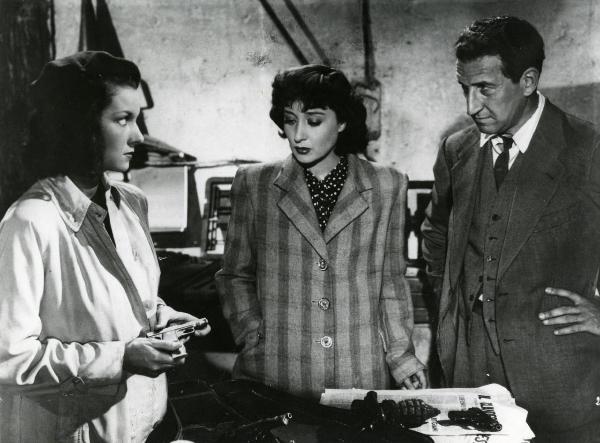 Scena del film "Due lettere anonime" - Regia Mario Camerini, 1945 - Dina Sassoli, sulla sinistra, mostra una pistola a Clara Calamai e Carlo Ninchi. Di fronte a loro un tavolo con sopra giornali e armi.