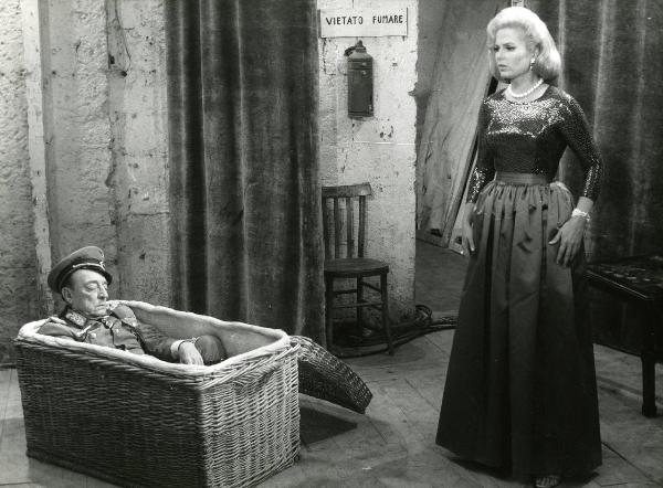 Scena del film "Due marines e un generale" - Regia Luigi Scattini, 1965 - Martha Hyer, in piedi, guarda Buster Keaton che dorme in un baule di vimini.