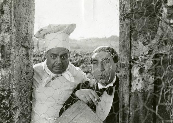 Scena del film "Due milioni per un sorriso" - Regia Carlo Borghesio, Mario Soldati, 1939 - Giuseppe Pierozzi, a sinistra, e Guido Barbarisi, a destra, osservano al di là di una rete di recinzione.