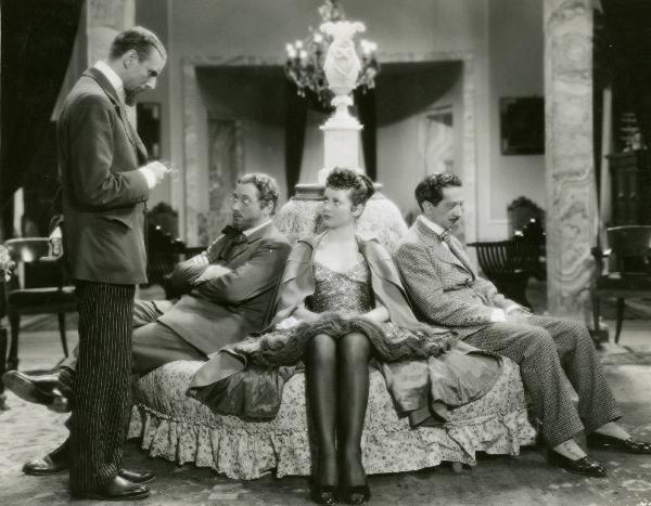 Scena del film "I due misantropi" - Regia Amleto Palermi, 1937 - Sergio Tofano, in piedi a sinistra, con occhiali in mano, parla a Nino Besozzi, María Denis, Enrico Viarisio, seduti su un divano.