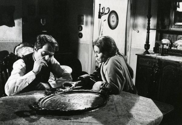 Scena del film "E cominciò il viaggio nella vertigine" - Regia Toni De Gregorio,1974 - Seduti a un tavolo: a destra, Ingrid Thulin conversa con Sergio Fantoni, a sinistra, intento a fumare una sigaretta.