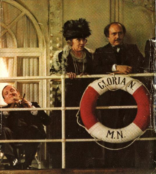 Scena del film "E la nave va" - Regia Federico Fellini, 1983 - A sinistra, Janet Suzman e un attore non identificato guardano dritto davanti a loro poggiati alla ringhiera della nave. Dietro, Peter Callier, seduto, osserva la scena fumando un sigaro.