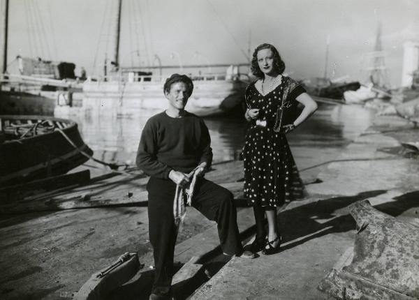 Scena del film "È sbarcato un marinaio" - Regia Piero Ballerini, 1940 - Figure intere di Amedeo Nazzari, a sinistra, e Germana Paolieri, a destra, sorridenti, in posa su una banchina portuale.