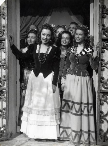 Scena del film "Elisir d'amore" - Regia Amleto Palermi, 1941 - A sinistra, Margherita Carosio, con lo sguardo rivolto verso sinistra e Jone Salinas, a destra. Dietro di loro, attori e attrici non identificati.