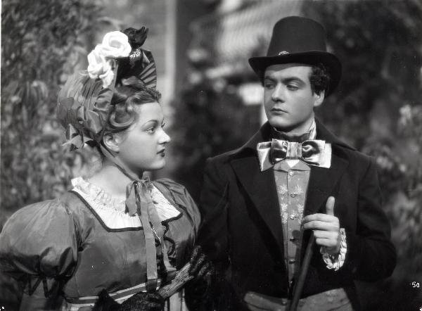 Scena del film "Elisir d'amore" - Regia Amleto Palermi, 1941- Giuseppe Rinaldi, a destra,con in mano un bastone, osserva un'attrice non identificata, a sinistra, di profilo che tiene in mano un ventaglio.