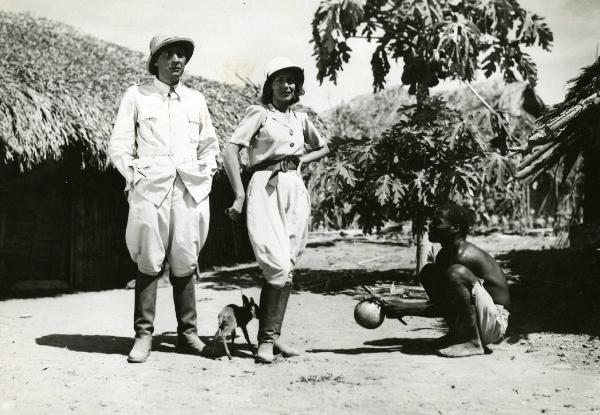 Scena del film "Equatore" - Regia Gino Valori, 1939 - A destra, Milena Penovich, con un piccolo cane al guinzaglio, e Cesare Fantoni, a sinistra, guardano dritto davanti a loro. Intanto, un attore non identificato, accovacciato a destra, li osserva.