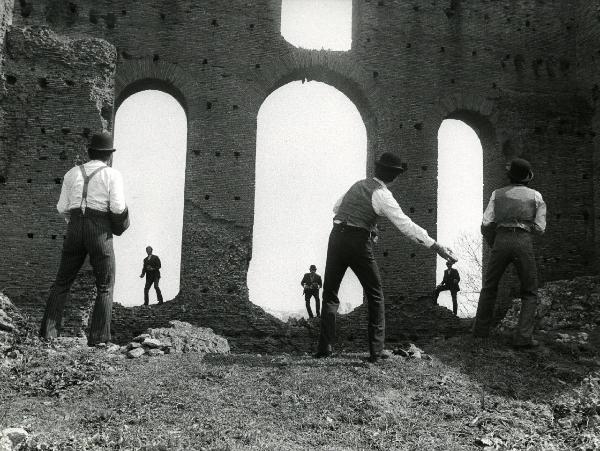 Scena del film "Er più storia d'amore e di coltello" - Regia Sergio Corbucci, 1971 - Benito Stefanelli, a sinistra, e due attori non identificati, guardano davanti a loro in direzione di Ninetto Davoli, a destra, e Adriano Celentano, al centro.