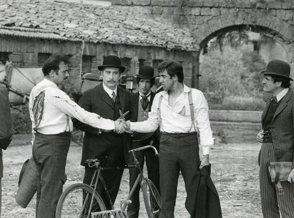 Scena del film "Er più storia d'amore e di coltello" - Regia Sergio Corbucci, 1971 - Al centro un attore non identificato, mentre Adriano Celentano e un attore non identificato si stringono la mano. Nino Davoli, a destra, li osserva.