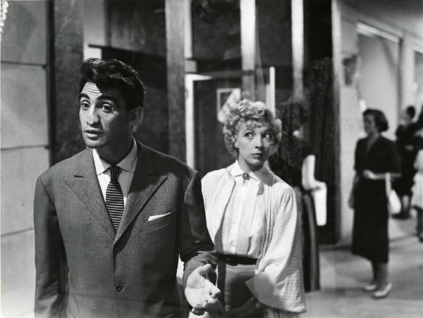 Scena del film "Era lui si si" - Regia Vittorio Metz, Marcello Marchesi, Marino Girolami, 1951 - Walter Chiari, con il naso premuto contro un vetro guarda davanti a sé. Isa Barzizza, alle sue spalle, lo osserva. Dietro, attrici non identificate.