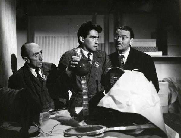 Scena del film "Era lui si si" - Regia Vittorio Metz, Marcello Marchesi, Marino Girolami, 1951 - Walter Chiari, al centro, regge con la mano una pila di bicchieri, una palla e un bicchiere ribaltato. Due attori non identificati, lo osservano.