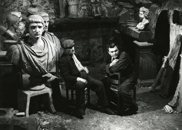 Scena del film "Era notte a Roma" - Regia Roberto Rossellini, 1960 - Serghej Bondarciuk e un attore non identificato, sono seduti su delle sedie. Il secondo osserva verso destra, il primo, rivolge lo sguardo davanti a sé.