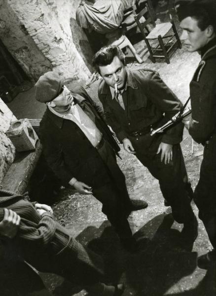 Scena del film "Era notte a Roma" - Regia Roberto Rossellini, 1960 - Serghej Bondarciuk, al centro con una sigaretta in bocca, guarda davanti a sè. Attorno, un altro attore non identificato, in abiti militari, imbraccia un fucile.