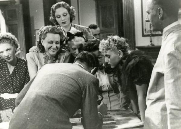 Scena del film "Eravamo 7 sorelle" - Regia Nunzio Malasomma, 1939 - Lotte Menas, Olivia Fried, al centro e alcuni attori non identificati osservano ciò che sta mostrando loro un attore non identificato con una lente di ingrandimento in mano.