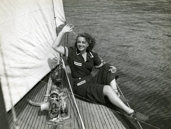 Scena del film "Eravamo 7 sorelle" - Regia Nunzio Malasomma, 1939 - Paola Barbara seduta sul ponte di una barca a vela, con una sigaretta nella mano sinistra, sorride e alza il braccio destro in gesto di saluto.