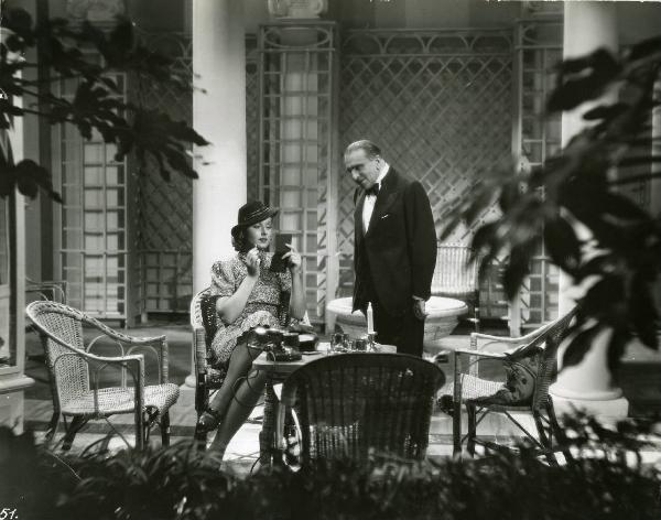 Scena del film "Eravamo 7 sorelle" - Regia Nunzio Malasomma, 1939 - Antonio Gandusio, in piedi leggermente proteso, osserva Paola Barbara seduta a un tavolo mentre è intenta a truccarsi guardandosi in un piccolo specchio.