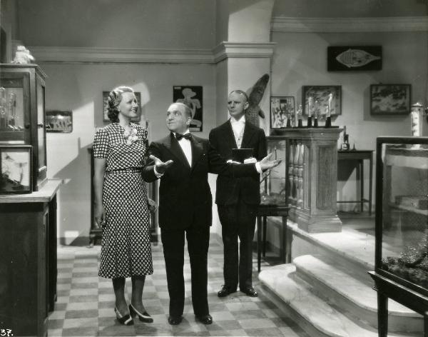 Scena del film "Eravamo 7 sorelle" - Regia Nunzio Malasomma, 1939 - Antonio Gandusio, al centro, rivolge lo sguardo verso Paola Barbara e tiene le braccia alzate. Intanto, dietro, Sergio Tofano osserva la scena.