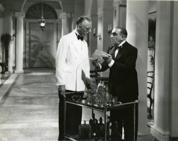 Scena del film "Eravamo 7 sorelle" - Regia Nunzio Malasomma, 1939 - Antonio Gandusio, a destra, mostra un foglio manoscritto a Sergio Tofano, a sinistra, in abiti da cameriere, che tiene le mani appoggiate a un carrello bar.