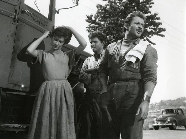 Scena del film "Esterina" - Regia Carlo Lizzani, 1959 - Di fianco a un autoveicolo: Geoffrey Horne, al centro, osserva a braccia conserte Carla Gravina. Intanto Domenico Modugno, a destra, rivolge lo sguardo verso destra.