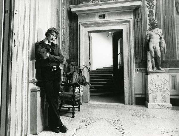 Scena del film "L'etrusco uccide ancora" - Regia Armando Crispino, 1972 - Figura intera di Alex Cord che guarda dritto davanti a sé mentre si avvicina il braccio sinistro al petto e si appoggia la mano destra sul collo.