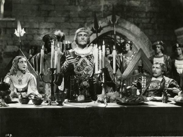 Scena del film "Ettore fieramosca" - Regia Alessandro Blasetti, 1938 - Mario Ferrari, a destra appoggiato al bracciolo della sedia, e Clara Calamai, a sinistra, osservano Osvaldo Valenti, al centro che tiene sollevato un calice.