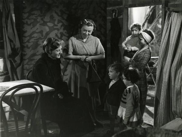 Scena del film "Europa 51" - Regia Roberto Rossellini, 1952 - Ingrid Bergman, seduta a sinistra, sorride a due giovani attori non identificati, mentre due attrici, una al centro e una a destra con in braccio un bambino, la osservano.