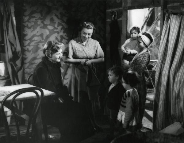 Scena del film "Europa 51" - Regia Roberto Rossellini, 1952 - Ingrid Bergman, seduta a sinistra, sorride a due giovani attori non identificati, mentre due attrici, una al centro e una a destra con in braccio un bambino, la osservano.