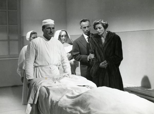 Scena del film "Europa 51" - Regia Roberto Rossellini, 1952 - Ettore Giannini stringe il braccio destro di Ingrid Bergman. Lei, osserva un attore non identificato steso su un letto, spinto da un altro attore non identificato nei panni di medico.