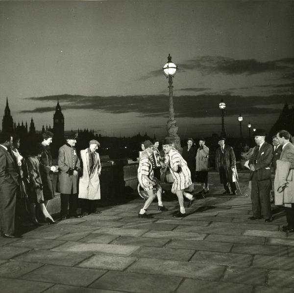 Scena del film "Europa di notte" - Regia Alessandro Blasetti, 1959 - Al centro, due attori non identificati, con indosso lunghe camice a righe e cappelli simili a fez, ballano sul lungo Tamigi osservati da numerosi altri attori non identificati.