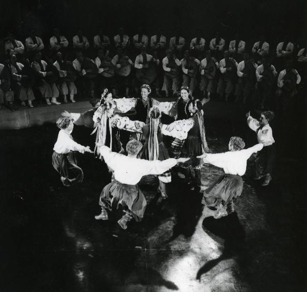 Scena del film "Europa di notte" - Regia Alessandro Blasetti, 1959 - Al centro i componenti del complesso Ukraina Orlych, in abiti folkloristici, sono intenti a ballare una danza tradizionale. In secondo piano li osserva un'orchestra di mandolini.