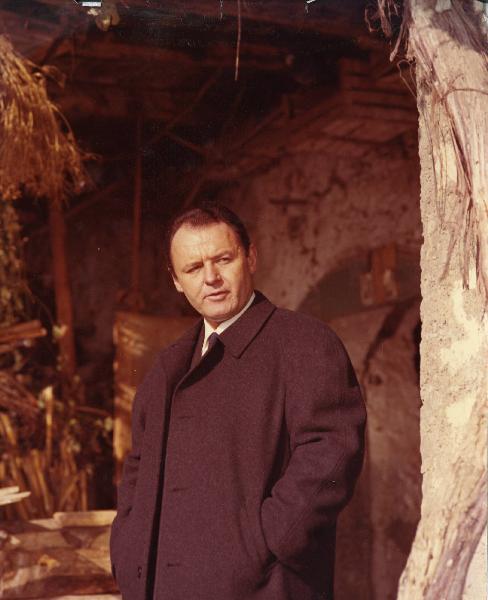 Scena del film "E venne un uomo" - Regia Ermanno Olmi, 1965 - Mezza figura di Rod Steiger che, con le mani nelle tasche del cappotto, rivolge lo sguardo verso destra.