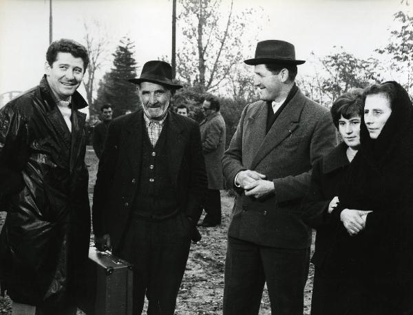 Scena del film "E venne un uomo" - Regia Ermanno Olmi, 1965 - In primo piano tre attori non identificati e due attrici non identificate. Il secondo uomo da sinistra tiene in mano una valigia.