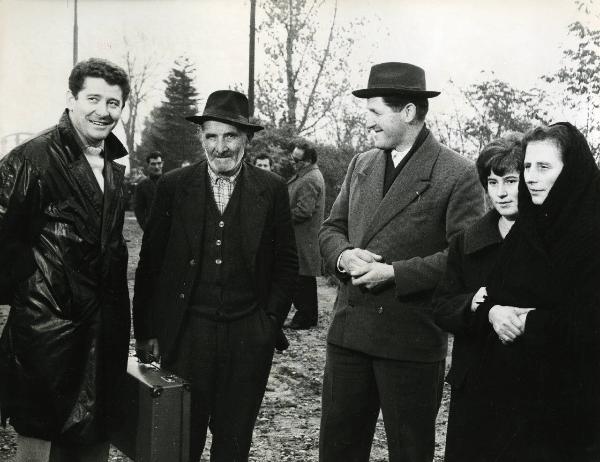 Scena del film "E venne un uomo" - Regia Ermanno Olmi, 1965 - In primo piano tre attori non identificati e due attrici non identificate. Il secondo uomo da sinistra tiene in mano una valigia.