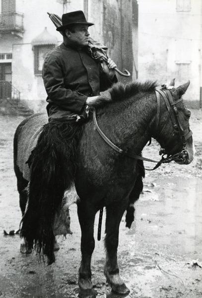 Scena del film "E venne un uomo" - Regia Ermanno Olmi, 1965 - In primo piano, un attore non identificato a cavallo guarda verso destra tenendo nella mano destra e sulla spalla un ombrello, mentre con la mano sinistra tiene le redini dell'animale.