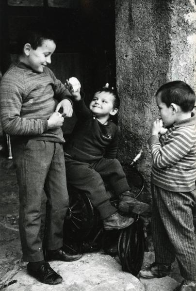 Scena del film "E venne un uomo" - Regia Ermanno Olmi, 1965 - Tre piccoli attori non identificati giocano tra di loro con dei pezzi di pane tra mani. Il bambino in centro è seduto sulla canna dell'acqua mentre quello a destra mangia un pezzo di pane.